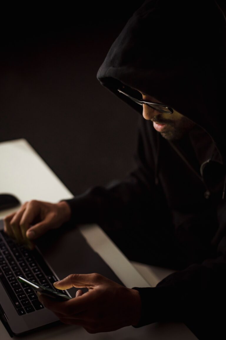 Person using a laptop and smartphone in a dark workspace